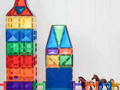 Colorful magnetic building tiles arranged into tower-like structures with toy horses nearby.