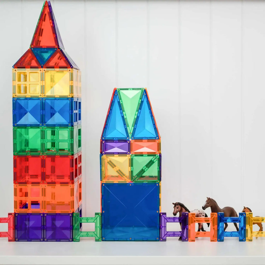 Colorful magnetic building tiles arranged into tower-like structures with toy horses nearby.