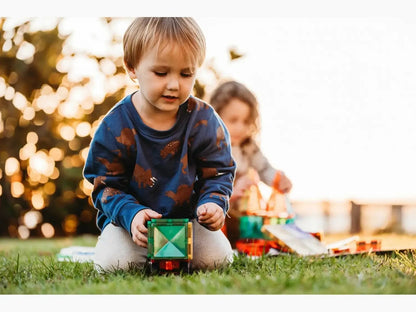 Young child playing with a colorful toy block on grass.
