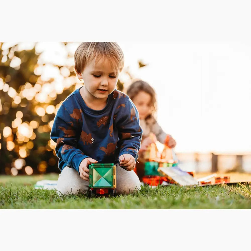 Young child playing with a colorful toy block on grass.