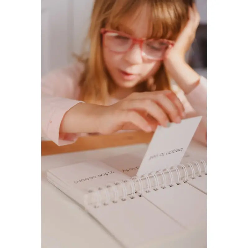 Person wearing red glasses writing in a spiral-bound notebook.