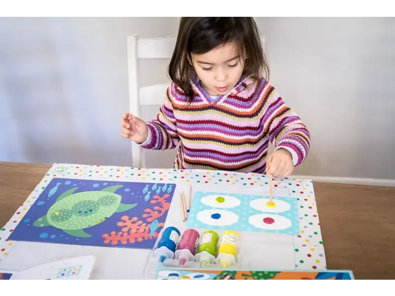 Child painting colorful artwork at a table with various art supplies.