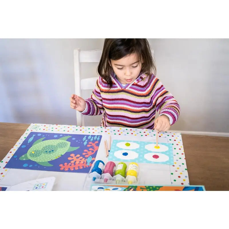 Child painting colorful artwork at a table with various art supplies.