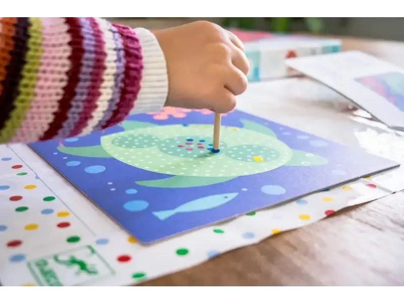 Colorful painting or craft project featuring a green circular shape with dots being created on blue paper.