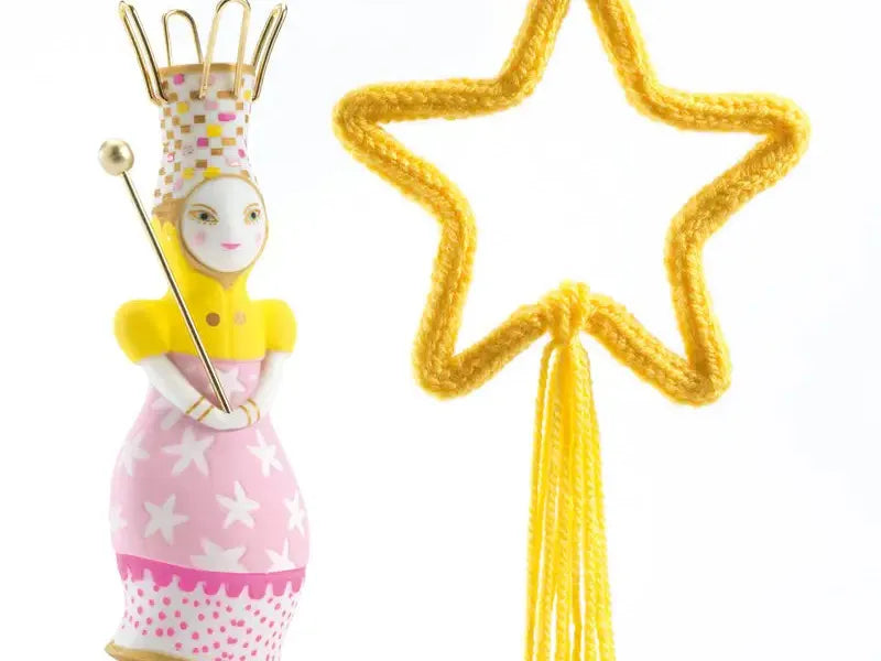 Whimsical fairy figurine with a crown, wand, and pink dress standing next to a yellow star-shaped object.