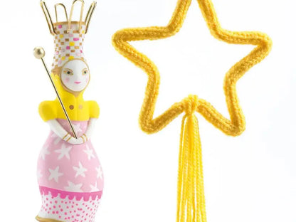 Whimsical fairy figurine with a crown, wand, and pink dress standing next to a yellow star-shaped object.