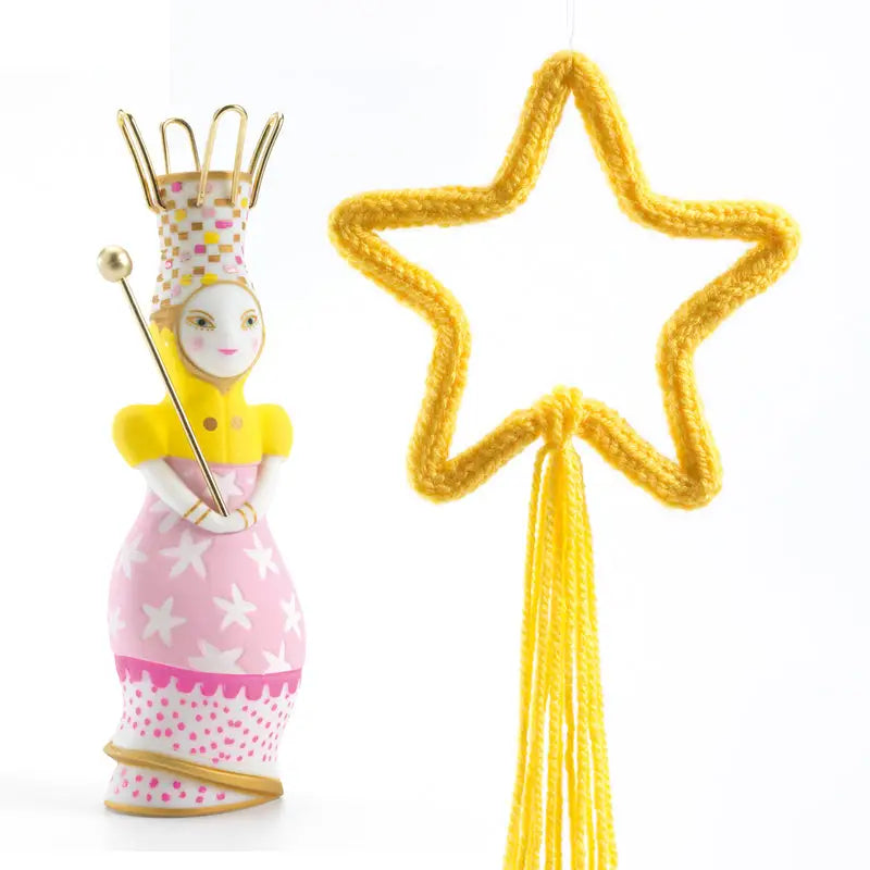 Whimsical fairy figurine with a crown, wand, and pink dress standing next to a yellow star-shaped object.