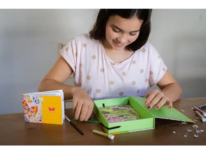 Young girl working on a craft project with a green tray and colorful materials.
