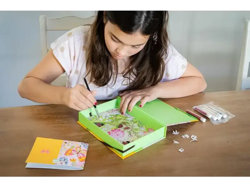 Girl working on a craft project with a green box and small pieces.
