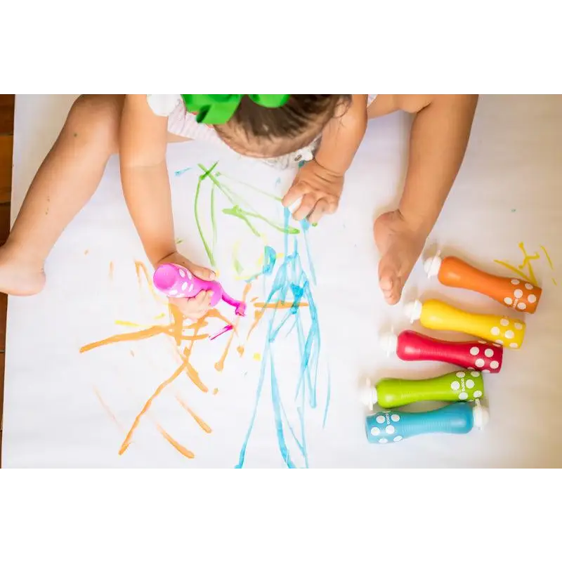 Child drawing with colorful chalk markers on a white surface.