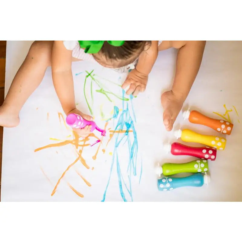 Child drawing with colorful chalk markers on a white surface.