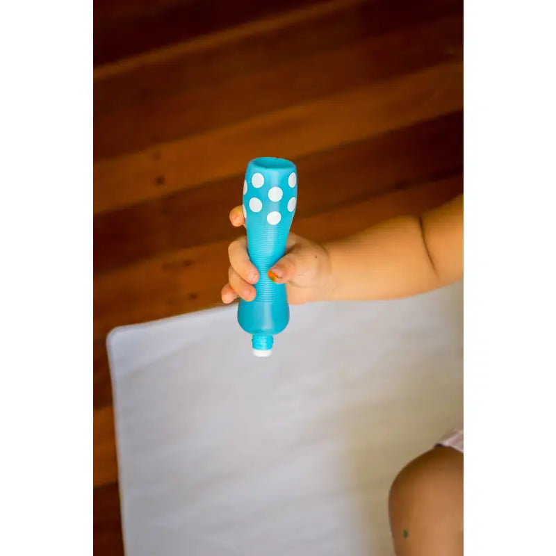 Blue plastic toy rattle with white polka dots held by a hand.