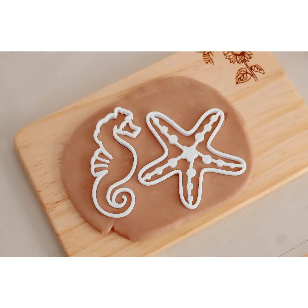 Cookie cutters shaped like a seahorse and a starfish on a wooden board.