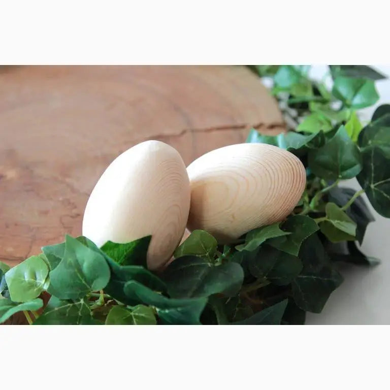 Two wooden eggs nestled among green ivy leaves.