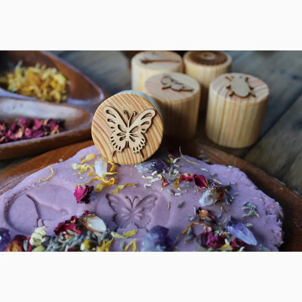 Wooden stamp with a butterfly design resting on purple clay or dough decorated with flower petals.