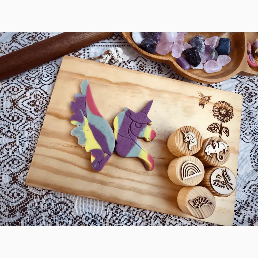 Wooden cutting board displaying colorful clay unicorn figures and round wooden stamps with nature designs.