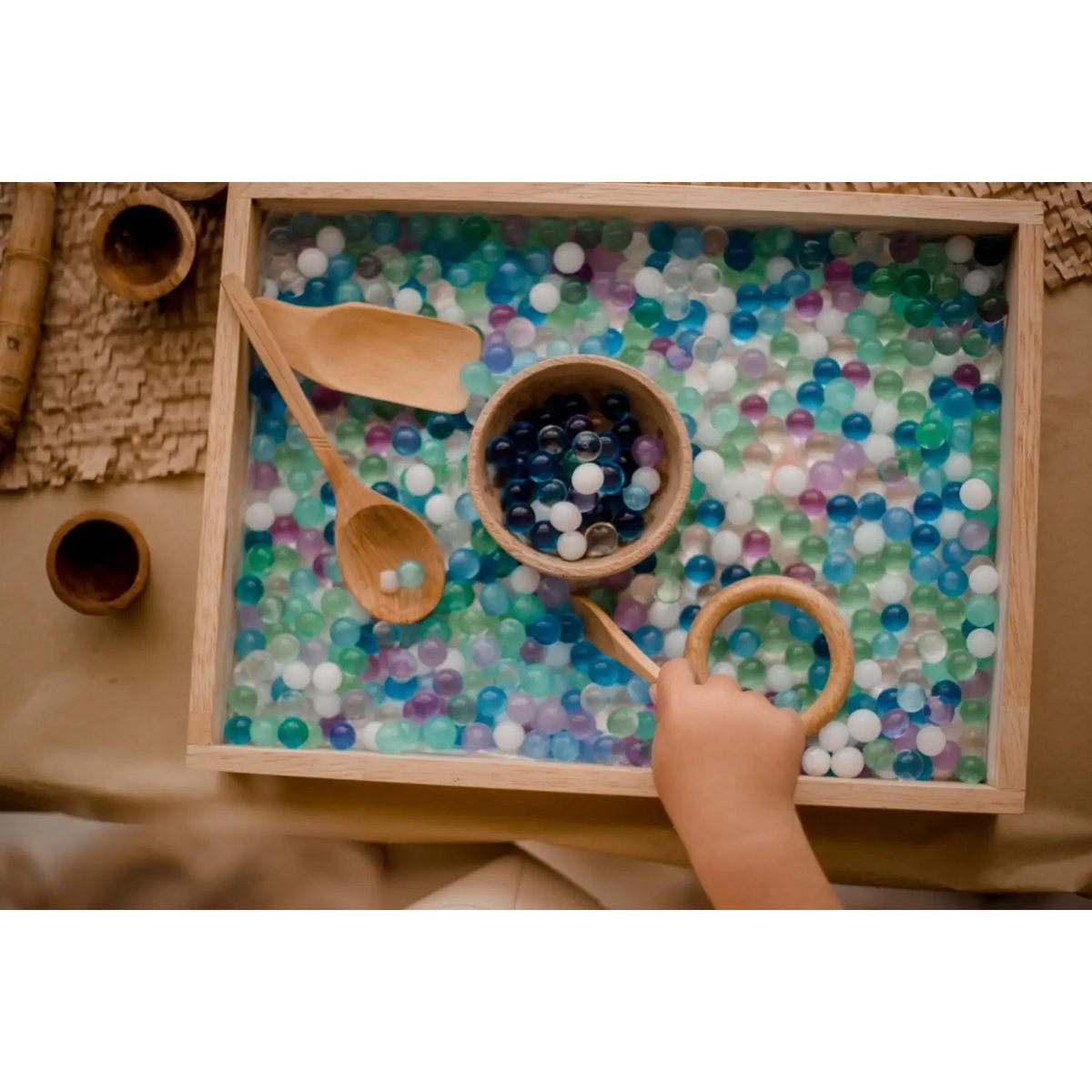 Sensory tray filled with colorful water beads and wooden scoops.