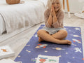 Child sitting cross-legged on a blue patterned play mat with hands clasped in front of their face.