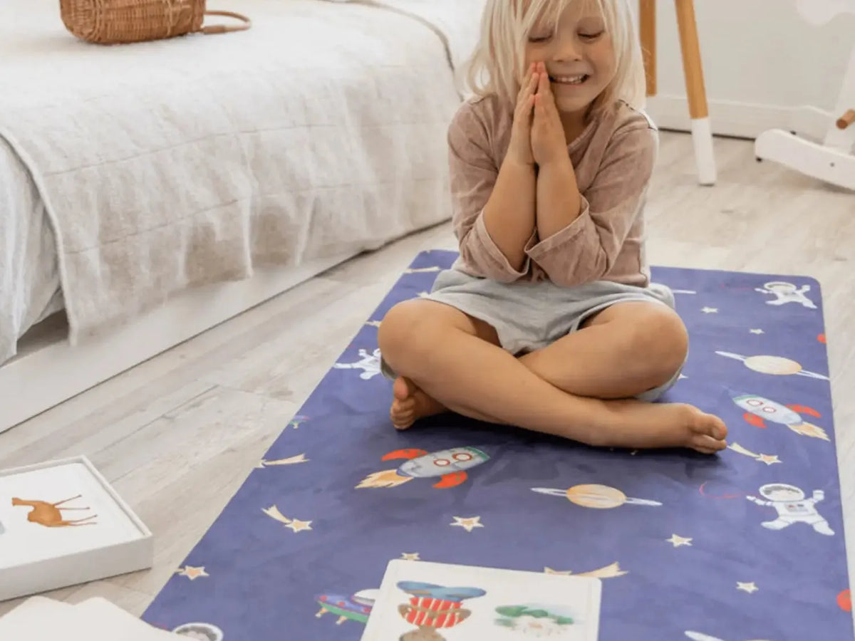 Child sitting cross-legged on a blue patterned play mat with hands clasped in front of their face.