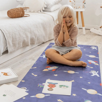 Child sitting cross-legged on a blue patterned play mat with hands clasped in front of their face.