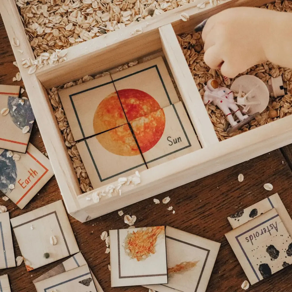 Wooden tray with compartments containing educational cards about celestial bodies and wood shavings.