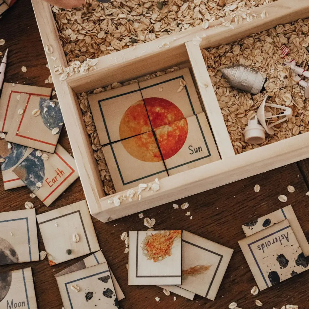 Wooden compartmentalized tray containing images of celestial objects and wood shavings.