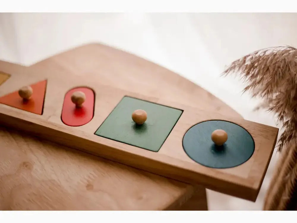 Wooden puzzle board with geometric shapes and knobs for grasping.
