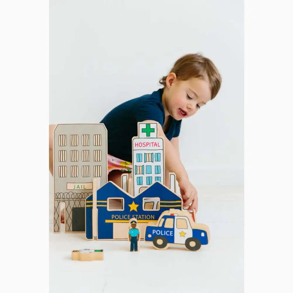 Wooden toy city playset featuring buildings and vehicles, including a police station and hospital.