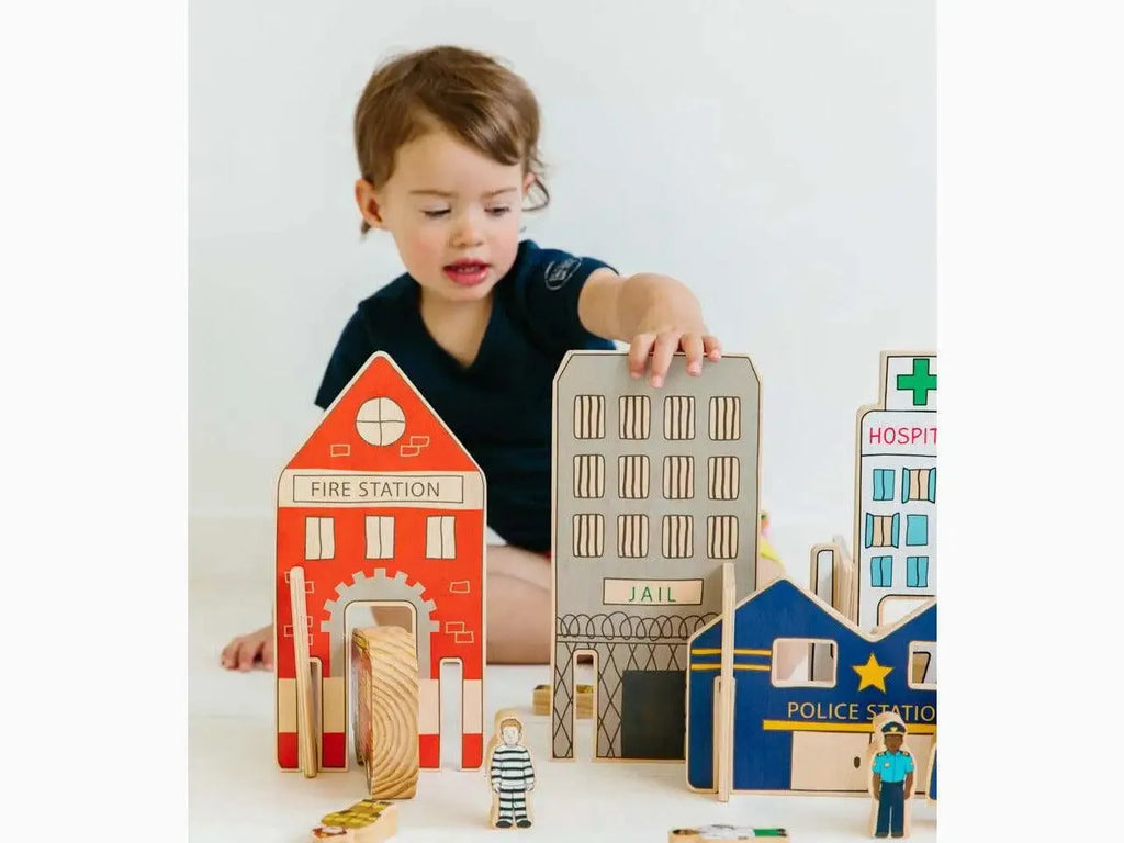 Child playing with wooden toy buildings and figurines representing a miniature town.