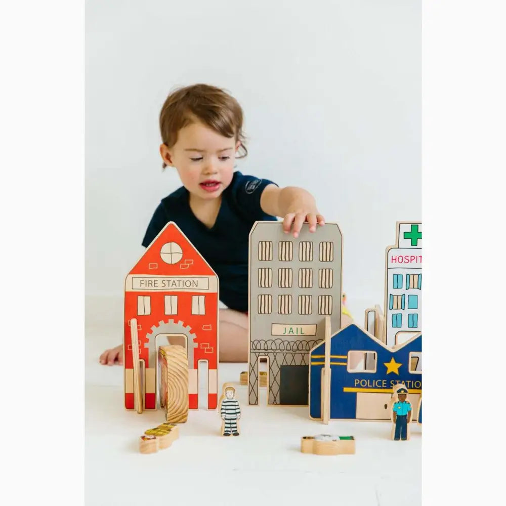 Child playing with wooden toy buildings and figurines representing a miniature town.