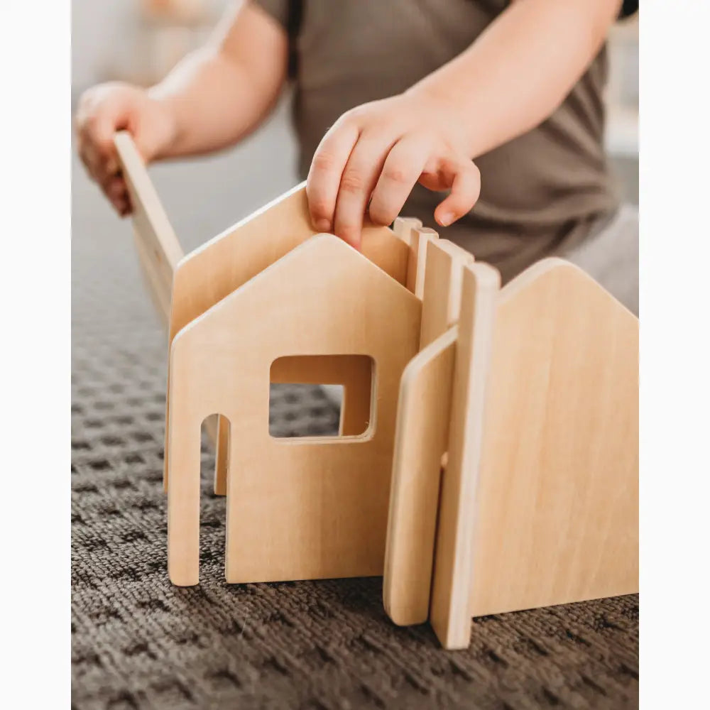 Wooden toy house with interlocking pieces being assembled by hands.