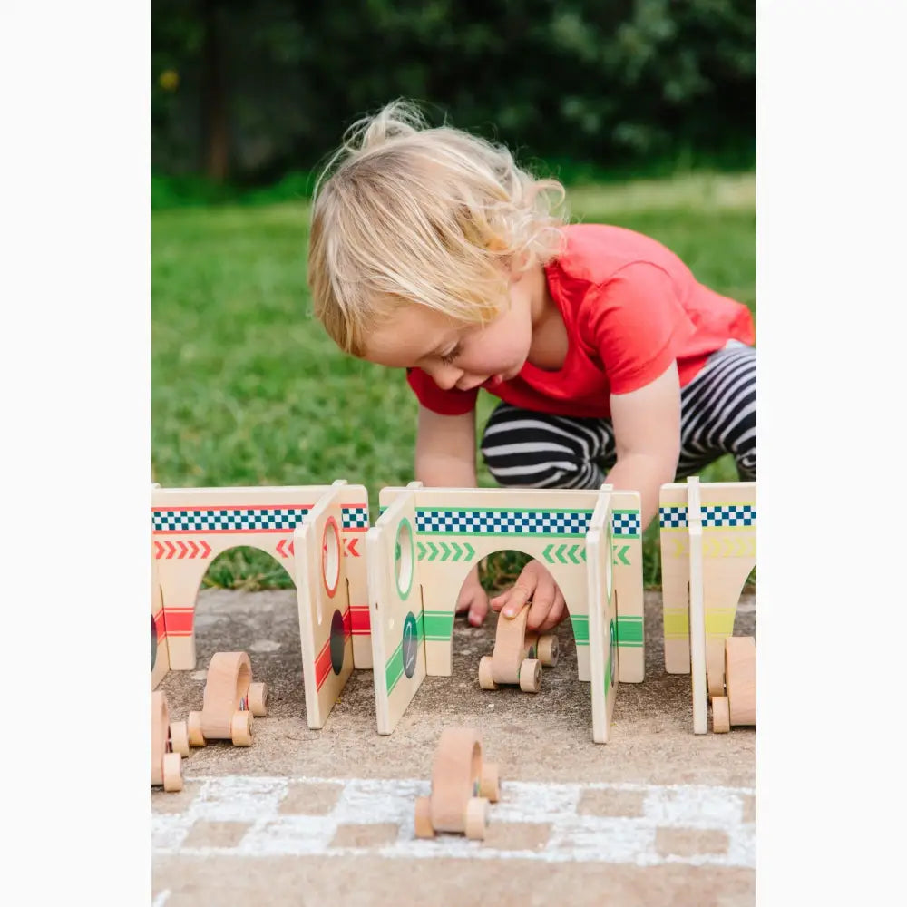 Child playing with a wooden toy race track or bridge structure on the ground.