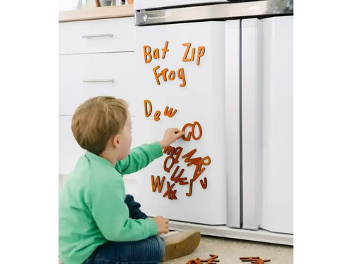 Child playing with magnetic letters on a refrigerator door.