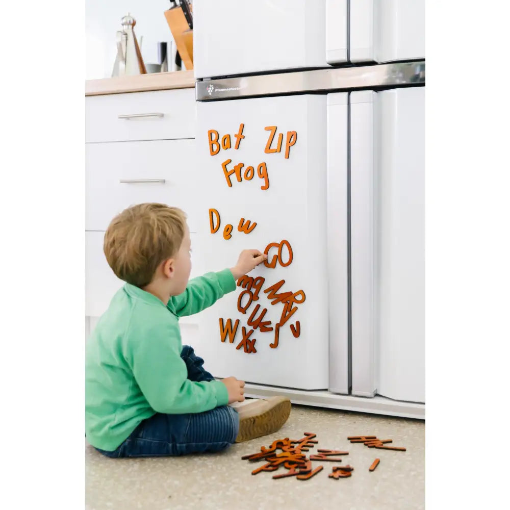 Child playing with magnetic letters on a refrigerator door.