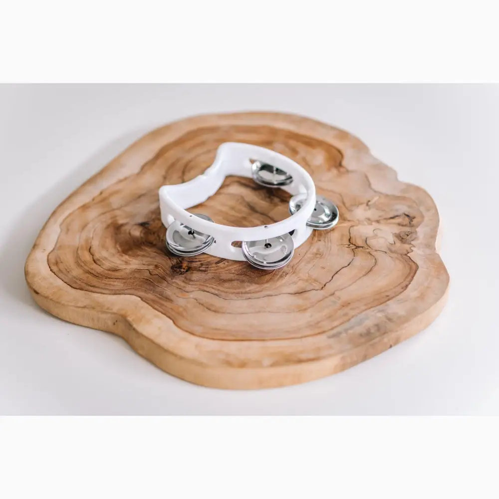 White tambourine resting on a wooden surface with visible tree rings.