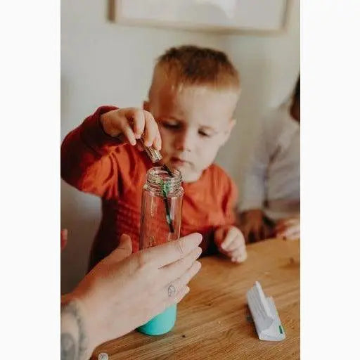 Young child in an orange shirt carefully placing something into a glass jar.