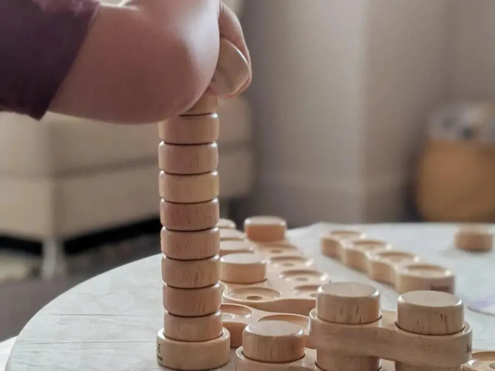 Wooden stacking toy with circular discs being assembled on a base.