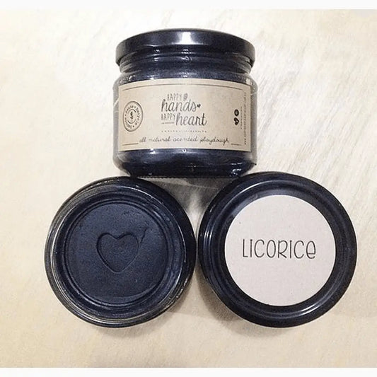 Glass jar with a label reading ’handle with heart’ alongside two smaller jar lids, one embossed with a heart shape and the other labeled ’licorice’.