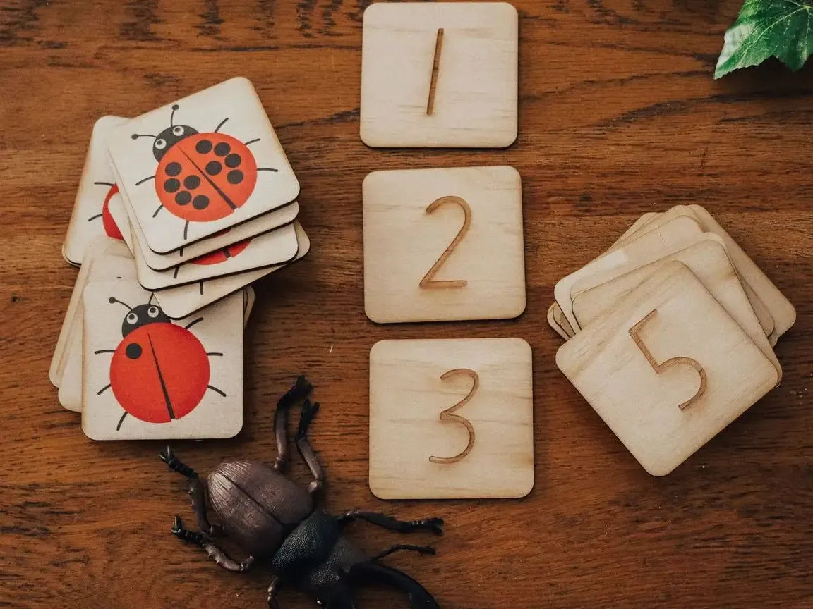 Wooden number tiles and insect-themed cards with a toy beetle on a wooden surface.