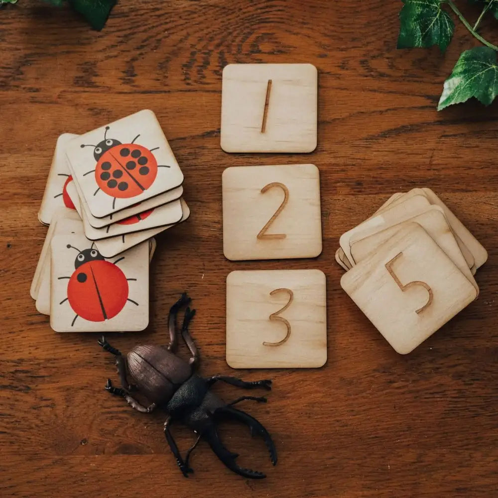 Wooden number tiles and insect-themed cards with a toy beetle on a wooden surface.