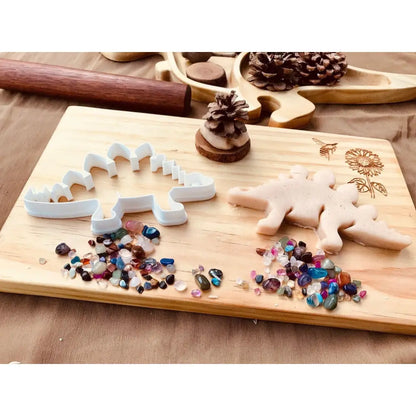 Wooden cutting board with dinosaur-shaped cookie cutters and colorful sprinkles.