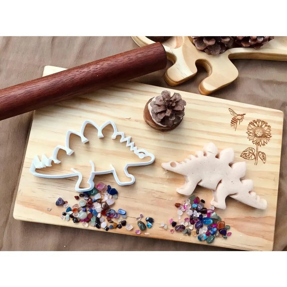 Wooden cutting board with dinosaur-shaped cookie cutters and colorful sprinkles.
