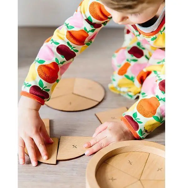 Colorful fruit-patterned long-sleeved shirt worn by someone manipulating wooden puzzle pieces.