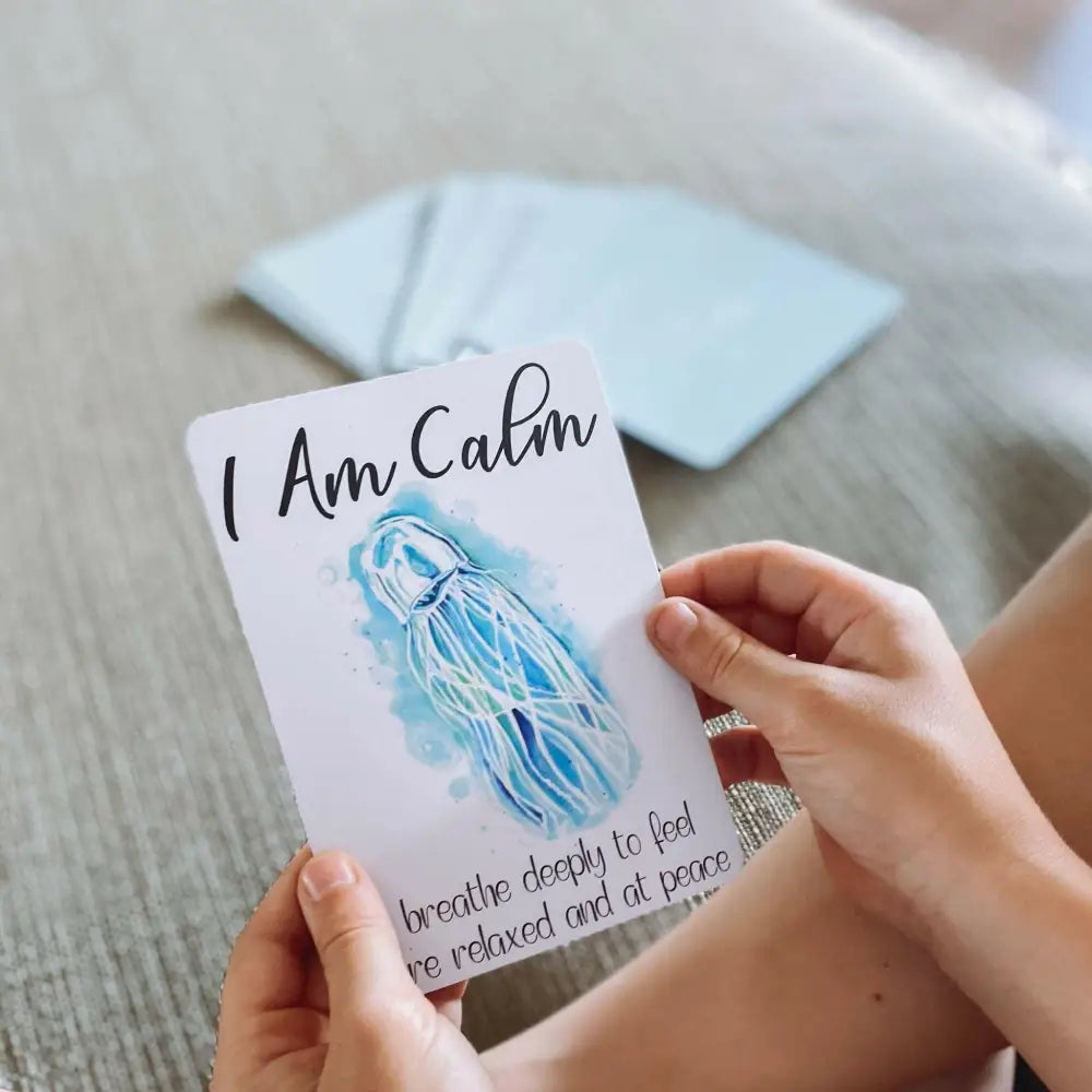 A card with ’I Am Calm’ text and a watercolor jellyfish illustration being held by hands.