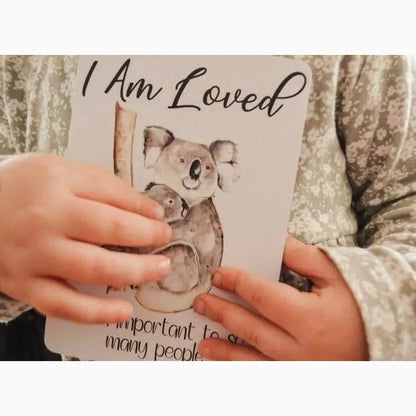 Book or card featuring an illustration of a koala and the text ’I Am Loved’ held by hands.