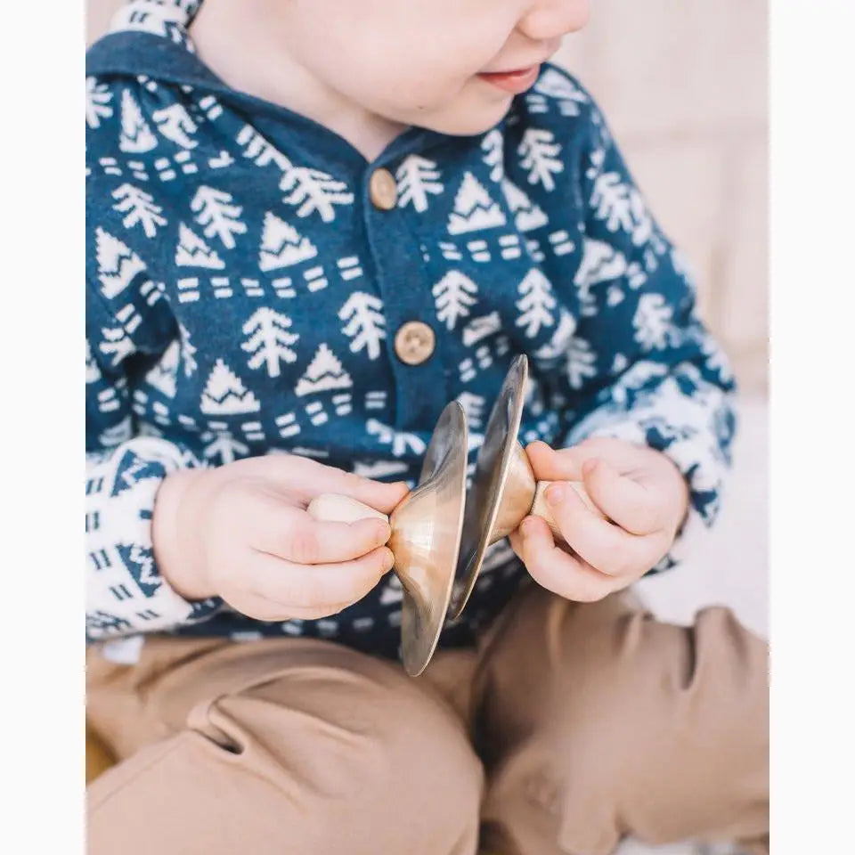 Pair of small cymbals or finger cymbals held by hands in a blue patterned sweater.