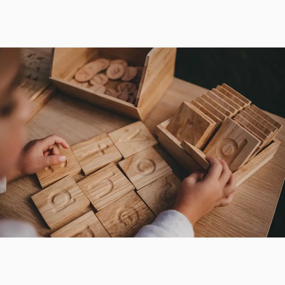 Wooden number blocks or tiles with carved numerals being handled by small hands.