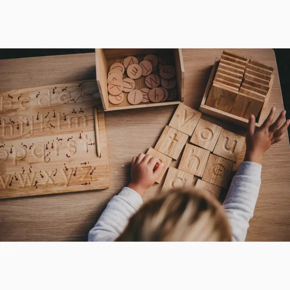 Wooden alphabet blocks and letter tiles being arranged by small hands on a table.