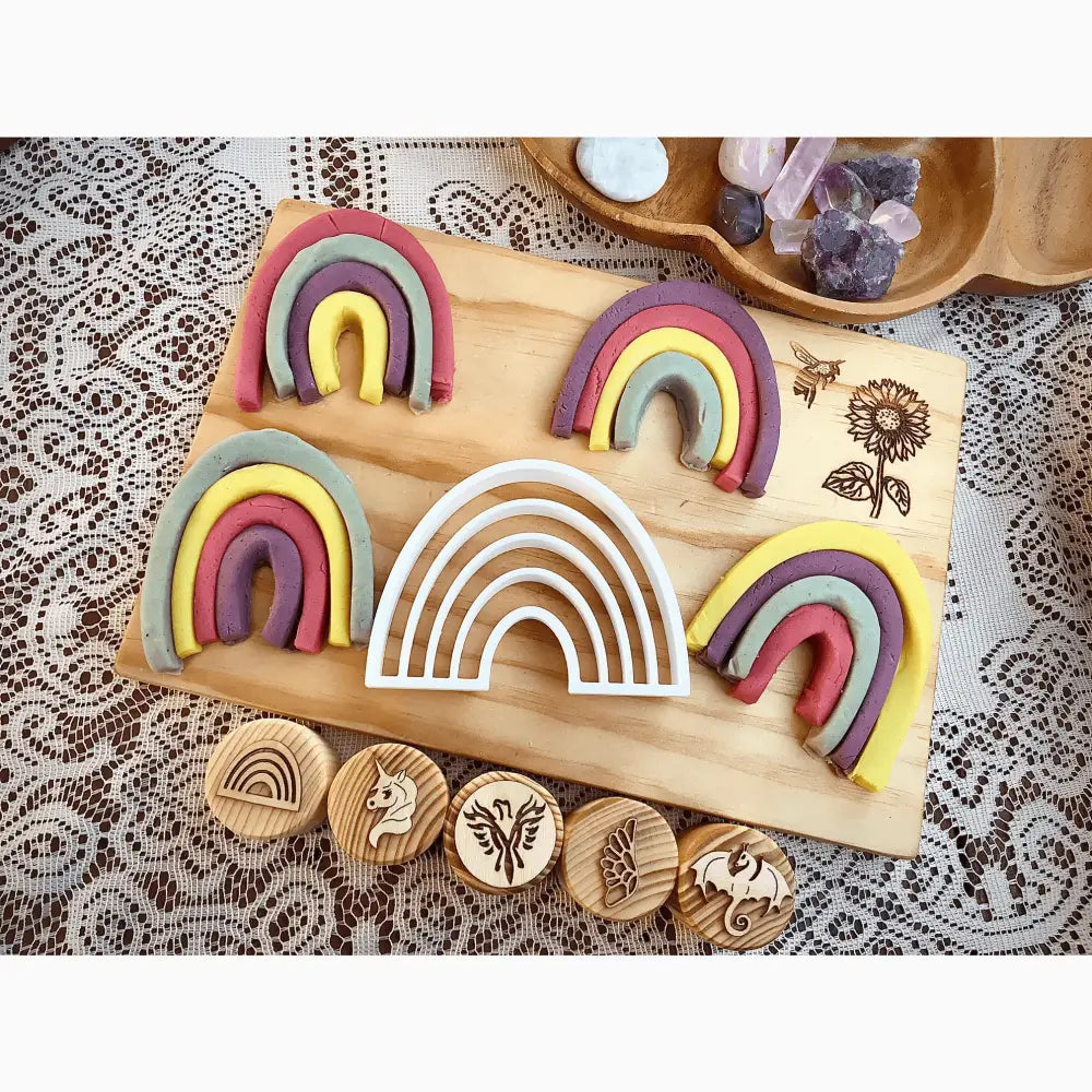 Wooden board displaying colorful rainbow-shaped clay or playdough arches alongside circular wooden stamps.