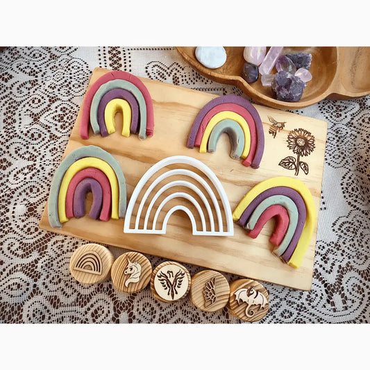 Wooden board displaying colorful rainbow-shaped clay or playdough arches alongside circular wooden stamps.